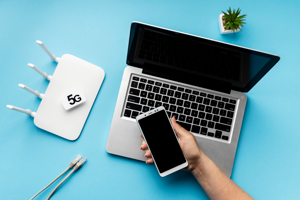 a router and a laptop lying on a table and a hand holding a mobile